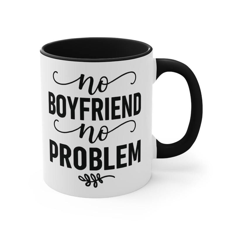 May include: White ceramic coffee mug with a black interior and handle. The mug features the text "no BOYFRIEND no PROBLEM" in a black, stylized font. A small floral design is at the bottom of the text.