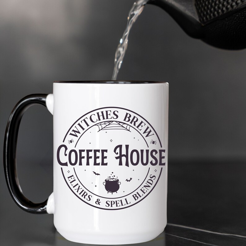 May include: White coffee mug with a black handle and black rim. The mug has a black and white graphic that says "Witches Brew Coffee House Elixirs & Spell Blends" with a cauldron and bats.