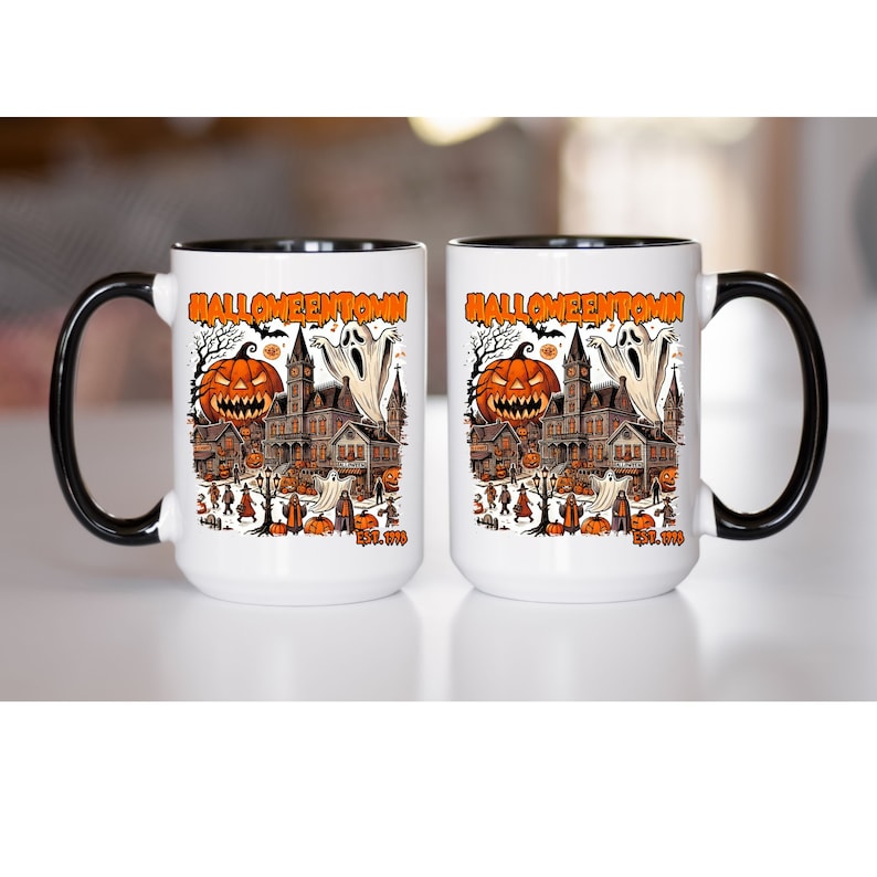 May include: Two white coffee mugs with black handles and black rims. Both mugs feature a Halloween-themed design with a haunted house, pumpkins, and ghosts. The text "Halloweentown Est. 1970" is printed on the front of each mug.