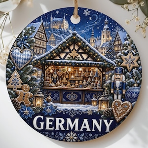 May include: A round ceramic ornament featuring a detailed illustration of a German Christmas market at night, with a nutcracker, gingerbread hearts, and snow-covered timber-framed buildings. The word GERMANY is printed in white at the bottom.