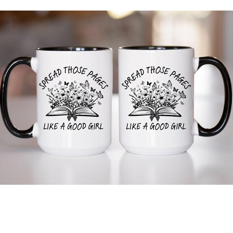 Puede incluir: Dos tazas blancas con asas y bordes negros. Cada taza presenta el texto "SPREAD THOSE PAGES LIKE A GOOD GIRL" sobre una ilustraci&oacute;n de un libro abierto con flores y mariposas.