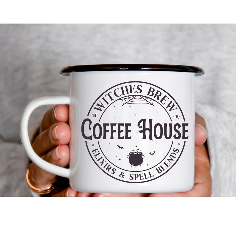 May include: White enamel mug with a black rim and handle. The mug has a black and white graphic of a witch's cauldron, bats, and a spider web with the text "Witches Brew Coffee House Elixirs & Spell Blends".