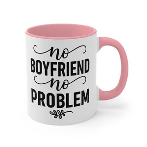 May include: White ceramic mug with a pink interior and handle. The mug features the text "no BOYFRIEND no PROBLEM" in black script. A small floral design is at the bottom of the text.