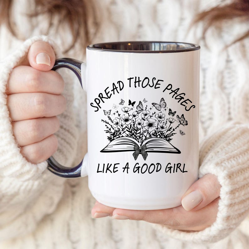 Puede incluir: Taza de cer&aacute;mica blanca con interior y asa negros. La taza presenta el texto "SPREAD THOSE PAGES LIKE A GOOD GIRL" con un gr&aacute;fico de un libro abierto, flores y mariposas.