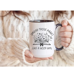 Puede incluir: Taza de cer&aacute;mica blanca con interior y asa negros. La taza presenta el texto "SPREAD THOSE PAGES LIKE A GOOD GIRL" con un dise&ntilde;o floral y de mariposas. Un regalo perfecto para los amantes de los libros.