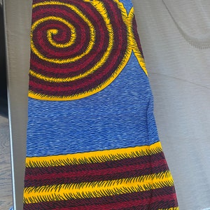 May include: A blue and yellow fabric with a spiral pattern in the center and horizontal stripes at the bottom.