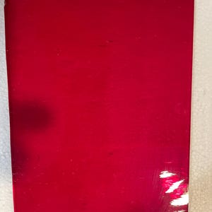 May include: A rectangular, solid red object with a glossy finish. The surface has minor scratches and imperfections. The edges are clean and defined. The object appears to be a piece of material or a component.