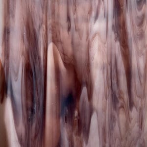 May include: A close-up of a piece of stained glass with a flowing, marbled pattern. The glass features shades of mauve, brown, and white, creating a dynamic, organic design. The letter "F" is visible in the upper left corner.