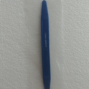 May include: A blue plastic tool, packaged in a clear plastic sleeve. The tool is labeled "CLASSIC AMERICAN TOOL" and is made in Taiwan. The tool is long and narrow, with a flat, angled end.