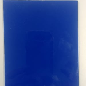 May include: A rectangular, glossy, cobalt blue object against a white background. The object's surface reflects light, creating highlights and shadows. The edges are clean and well-defined, suggesting a manufactured item. The overall appearance is simple and modern.