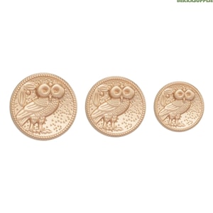 Może przedstawiać: Trzy złote metalowe guziki z wzorem sowy. Guziki są w różnych rozmiarach.