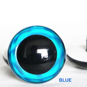 May include: Close-up of two blue doll eyes with a black pupil. The eyes have a vibrant blue and turquoise outer ring. One eye is in focus, while the other is slightly blurred. The word "BLUE" is printed in blue text below the eyes.