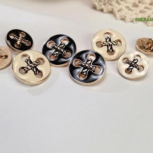 May include: Assortment of gold-tone buttons with black and white enamel and a rope design. The buttons have four holes.
