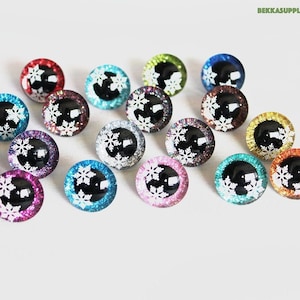 Op de afbeelding: Assortiment van 16 ronde, glinsterende glazen ogen met een zwart centrum en een wit sneeuwvlokkenontwerp. De ogen zijn in verschillende kleuren, waaronder rood, blauw, groen, goud, zilver en roze.