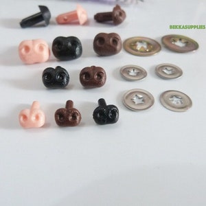 May include: A collection of small, plastic craft supplies, including various colors of doll noses and safety eyes, along with metal washers. The noses are in shades of pink, brown, and black. The text "BEKKASUPPLIES" is visible in the upper right corner.