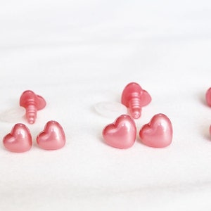 May include: A set of pink heart-shaped plastic safety eyes for plush toys. The eyes come in different sizes and have a shiny finish.