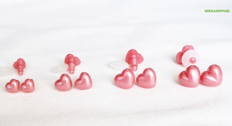 May include: A set of pink heart-shaped plastic safety eyes for plush toys. The eyes come in different sizes and have a shiny finish.