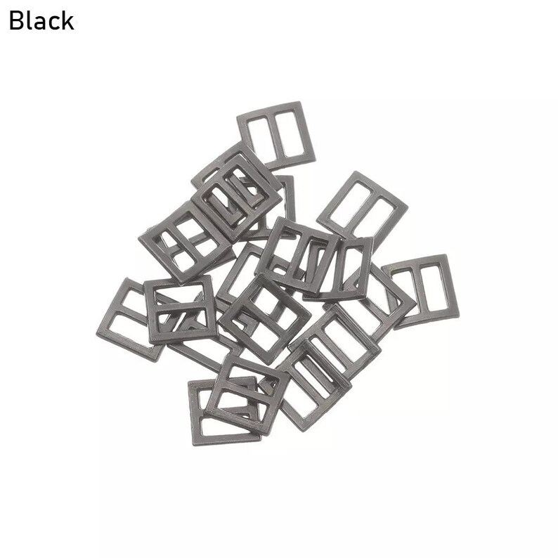 Op de afbeelding: Een stapel zwarte metalen schuifgespen. De gespen zijn vierkant met een rechthoekige opening in het midden.