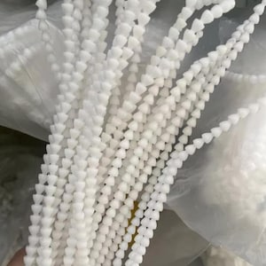 Może przedstawiać: Pęczek białych plastikowych opasek kablowych, każda z serią małych, trójkątnych główek. Opaski są elastyczne i wydają się nowe, o czystym, jasnym białym kolorze. Prawdopodobnie służą do porządkowania i zabezpieczania przedmiotów.