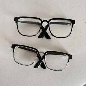 May include: Two pairs of eyeglasses with clear lenses. One pair has black frames, and the other has black frames with silver-colored rims. The glasses are rectangular and have a classic design.