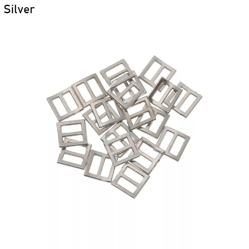 Op de afbeelding: Een stapel zilverkleurige metalen schuifgespen. De gespen zijn rechthoekig met een kleine opening in het midden.