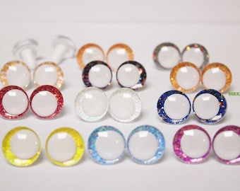May include: A collection of colorful, round doll eyes with white centers and glittery rims. The eyes come in various colors, including red, orange, yellow, blue, and purple. Some eyes have clear plastic posts.