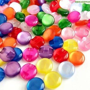 Op de afbeelding: Assortiment van kleurrijke plastic knopen met een reliëfdesign. De knopen zijn rond en hebben een glanzende afwerking.