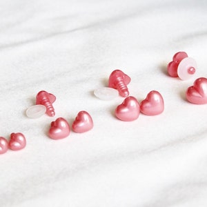 May include: Assortment of pink heart-shaped plastic safety eyes with white plastic washers and screws for plush toy making.