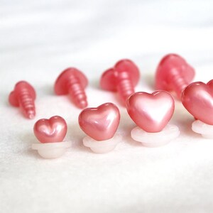 May include: A set of pink heart-shaped plastic safety eyes for crafts. The eyes come in various sizes and have a shiny finish.