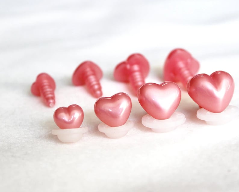 May include: A set of pink heart-shaped plastic safety eyes for crafts. The eyes come in various sizes and have a shiny finish.
