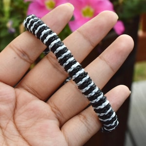 May include: A black and white striped bracelet made of woven cord.