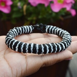May include: Black and white striped bracelet made of woven cord.