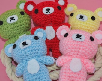 May include: Five crocheted teddy bears in different colours: green, red, yellow, blue and pink. Each bear has black eyes and a white tummy.