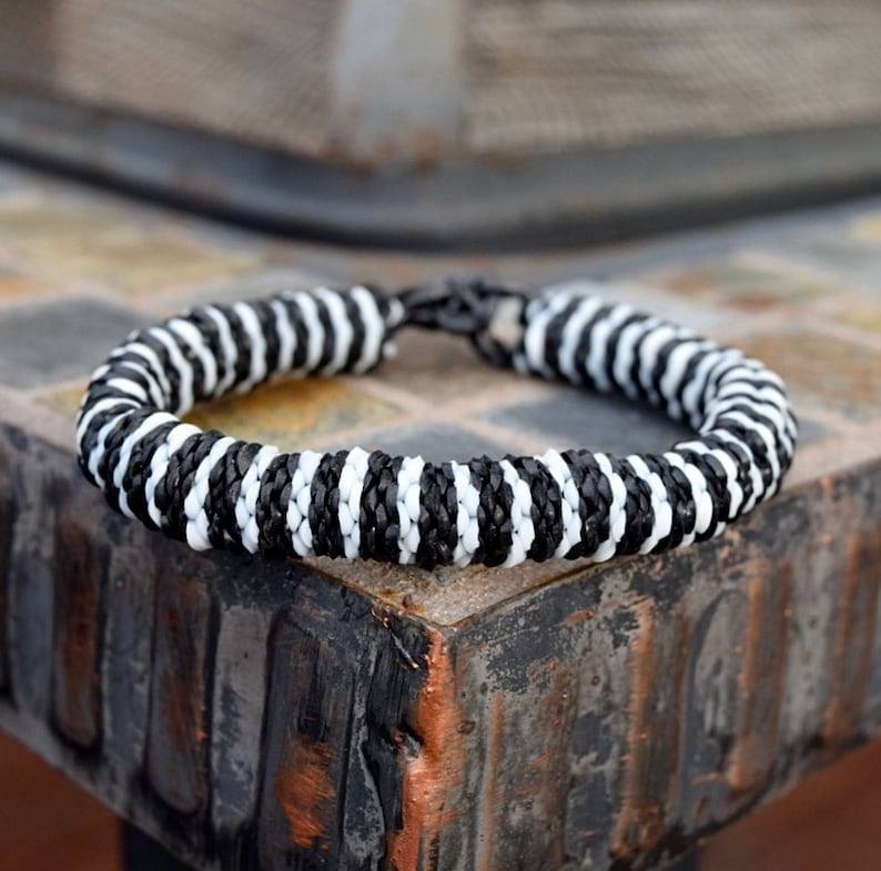 May include: Black and white striped bracelet made of woven cord. The bracelet has a metal clasp.