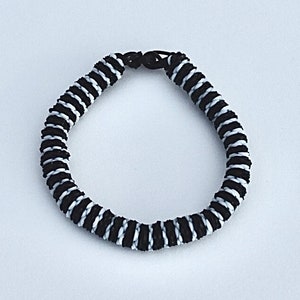 May include: Black and white braided bracelet with a simple clasp.