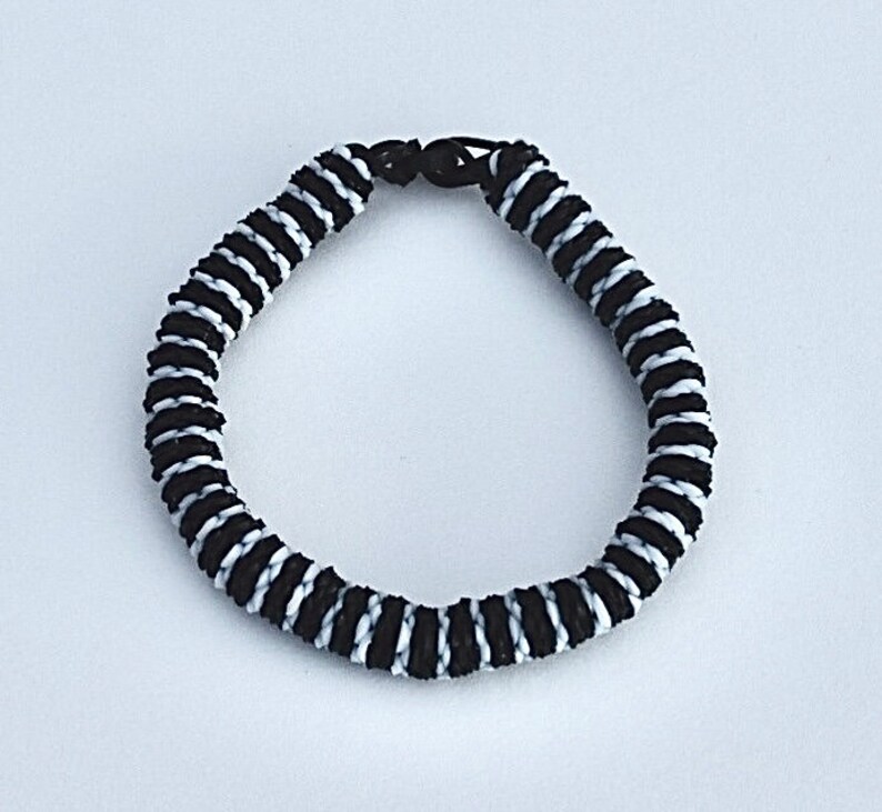 May include: Black and white braided bracelet with a simple clasp.