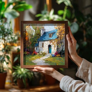 Op de afbeelding: Een ingelijst schilderij van een schilderachtig huisje met een blauw dak en een turkooizen deur. Het kunstwerk heeft een getextureerde, impressionistische stijl met levendige kleuren groen, geel en rood. De lijst heeft een warme bruine kleur.