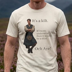 May include: A cream-colored short-sleeve t-shirt featuring a graphic of a person in a kilt with the text: It's a kilt. If I wore underwear then it would be a skirt. Och Aye! The shirt is worn with a blue, green, and red plaid kilt with a sporran.