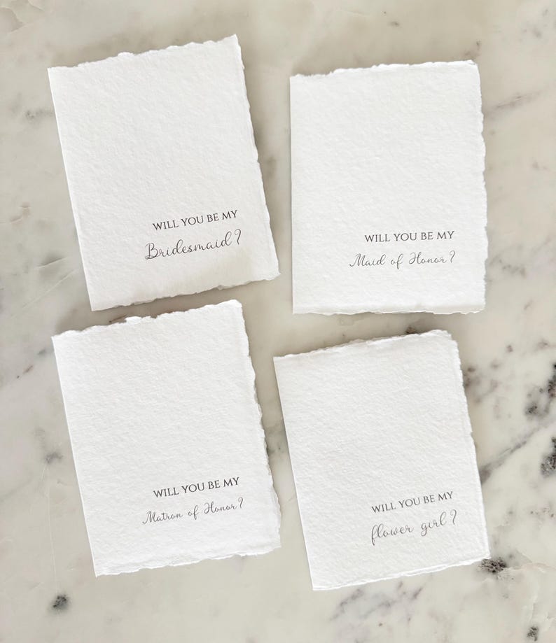 May include: Four white rectangular cards with deckled edges. Each card has the phrase "WILL YOU BE MY" followed by a different title: "Bridesmaid?", "Maid of Honor?", "Matron of Honor?", and "flower girl?" in elegant script.