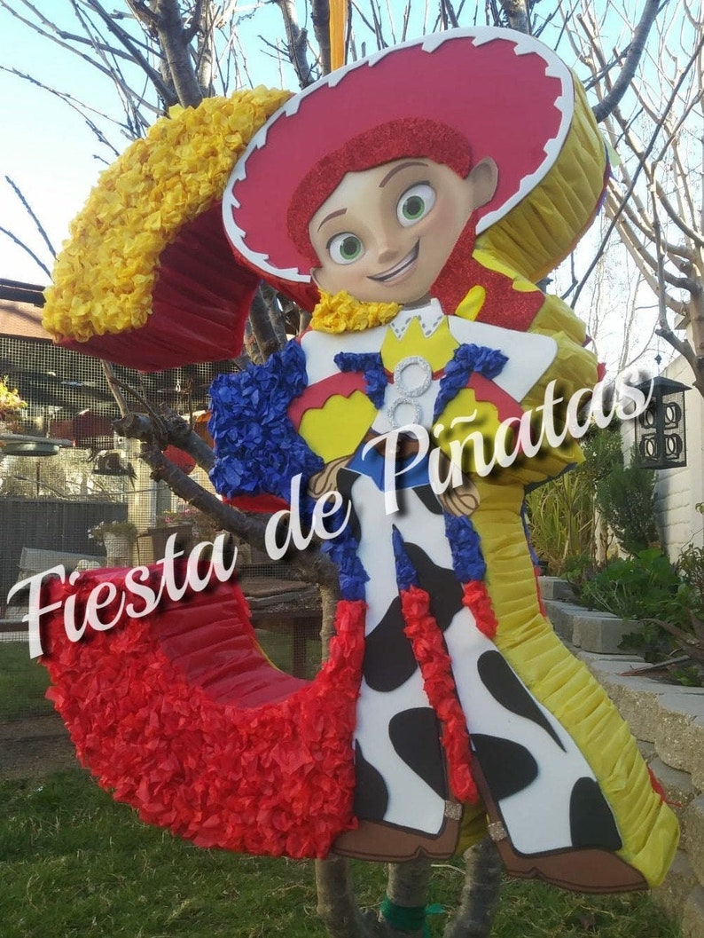 May include: A red, yellow, and blue pinata shaped like a cartoon character wearing a cowboy hat. The pinata is decorated with tissue paper and has the text "Fiesta de Pi&ntilde;atas" on it.