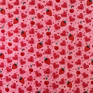 May include: Pink fabric with a repeating pattern of red hearts, strawberries, and cherries. The hearts are outlined in a darker red and have a swirl design.