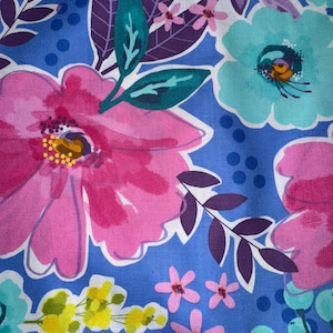 May include: A vibrant floral pattern featuring large pink and turquoise flowers with white outlines, set against a blue background dotted with darker blue circles. Purple leaves and smaller pink and yellow blossoms complete the design.