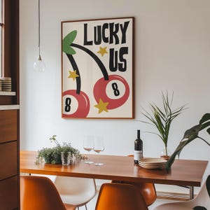 Może przedstawiać: Wydruk w ramie z retro wzorem przedstawiający dwie czerwone wiśnie z numerem 8 na nich. Wiśnie są na łodygach z zielonymi liśćmi, a nad nimi widnieje napis "LUCKY US". Wydruk jest na białym tle z ż&oacute;łtymi gwiazdami.