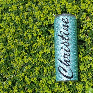 May include: A turquoise tumbler with a clear lid, covered in rhinestones and the name "Christine" written in black lettering.