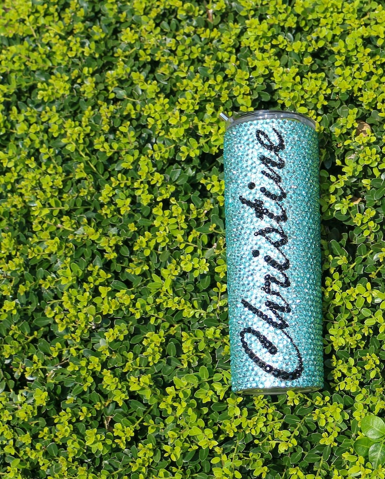May include: A turquoise tumbler with a clear lid, covered in rhinestones and the name "Christine" written in black lettering.