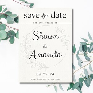 Op de afbeelding: Save the date kaart met een witte achtergrond en zwarte tekst. De kaart heeft een eenvoudig bloemenkransontwerp en de tekst "save the date" voor de bruiloft van Shawn & Amanda. De datum is 09.22.24 en de tekst "more information to come" staat onderaan.