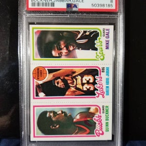 May include: A 1980 Topps basketball card set featuring three NBA players: Quinn Buckner, Kareem Abdul-Jabbar, and Mike Gale. The cards are graded NM-MT 8 and have a PSA authentication sticker.
