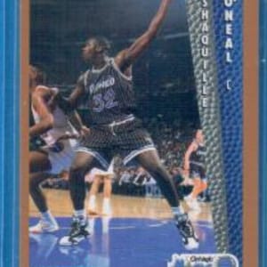 May include: A basketball trading card featuring a player in a blue and white jersey with the text "Orlando Magic" and "Shaquille O'Neal" on the card. The player is wearing a blue and white jersey with the number 32 on the front. The card is from the 1992-93 Fleer series.