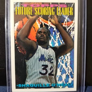 May include: A basketball trading card featuring a photo of Shaquille O'Neal in a blue and white Orlando Magic jersey with the number 32 on the front. The card has a white background with the text "Future Scoring Leader" in yellow and pink letters.