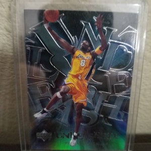 May include: A silver and black trading card featuring a basketball player in a yellow and purple jersey with the number 8 on the front. The player is jumping in the air with a basketball in his hands. The card has a holographic finish and the text "Upper Deck" and "Kobe Bryant" on the bottom.